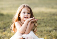 Cute Child Girl 3 4 Year Old Sitting In Field Wearing Dress Outdoors. Looking Away. Childhood.