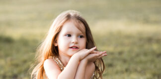 Cute Child Girl 3 4 Year Old Sitting In Field Wearing Dress Outdoors. Looking Away. Childhood.