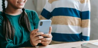 Stock photo of a tween girl smiling as she uses a cell phone at a table.