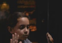 A child holding their hand up to a tank with a snake in it