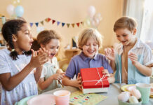 Diverse group of happy children at Birthday party with excited boy opening presents