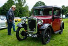 A man in a hat stands next to an antique car