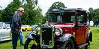 A man in a hat stands next to an antique car